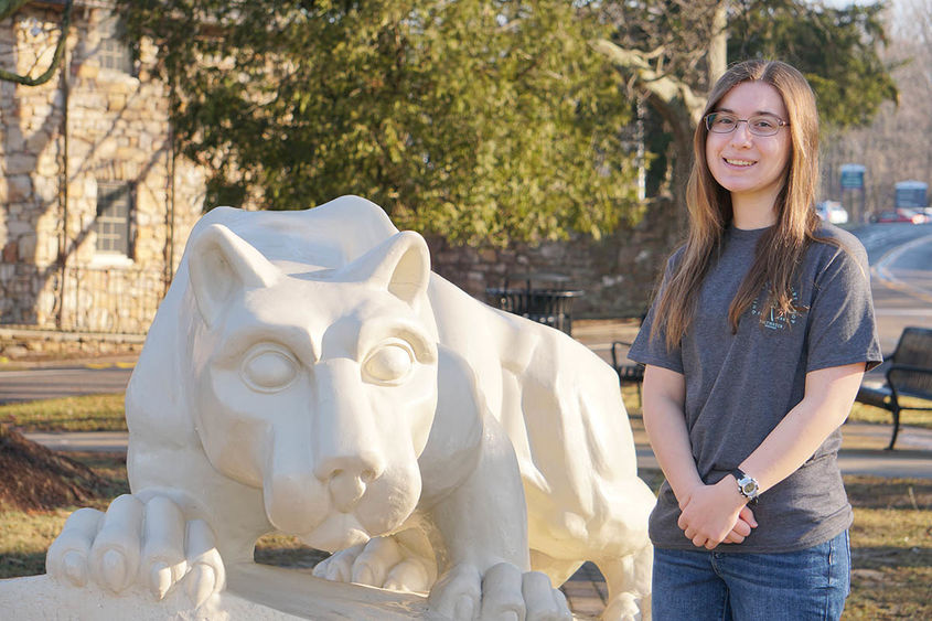 Female student standing outdoors next to Nittany Lion statue.