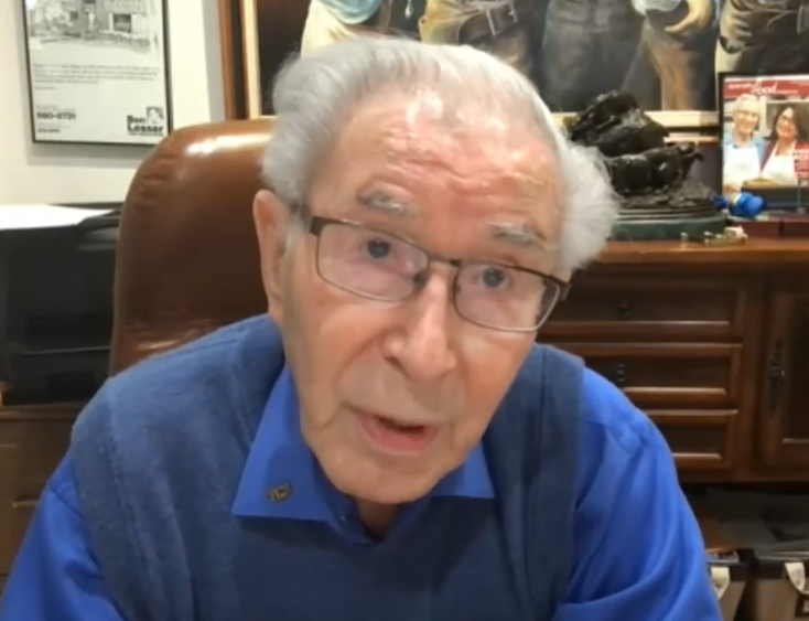 Man in a blue shirt and vest seated in a leather office chair.