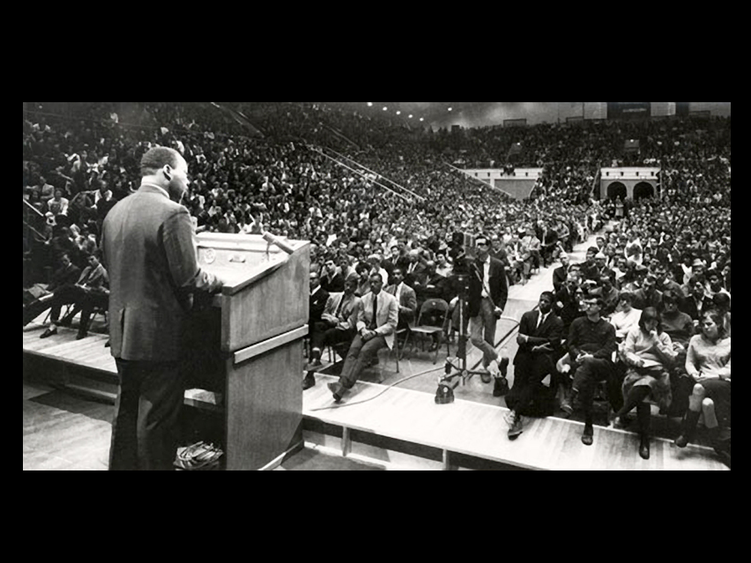 A black and white photo of Martin Luther King Jr. speaking at Rec Hall to a large audience