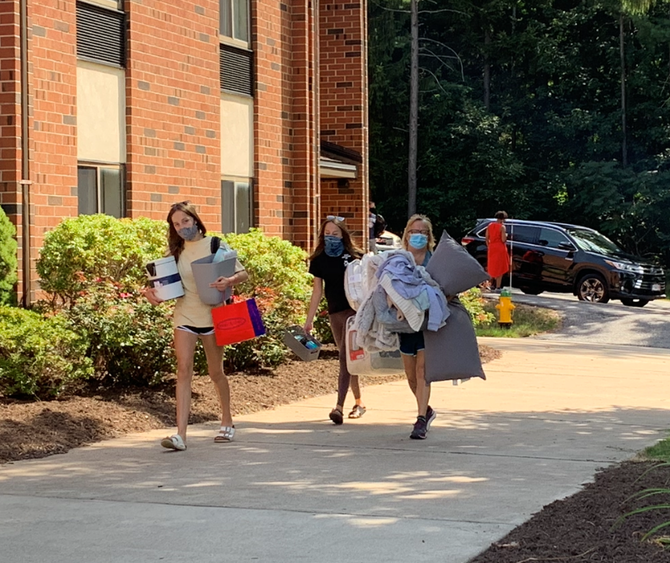 Students and a parent carrying boxes and other belongings on a sidewalk into North Hall