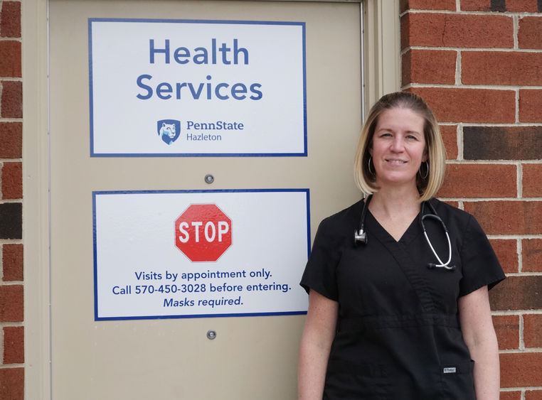 Woman in scrubs standing in front of office door with signs denoting campus health services.