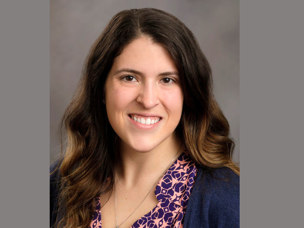 Woman with long dark hair in a floral blouse with navy blue sweater.