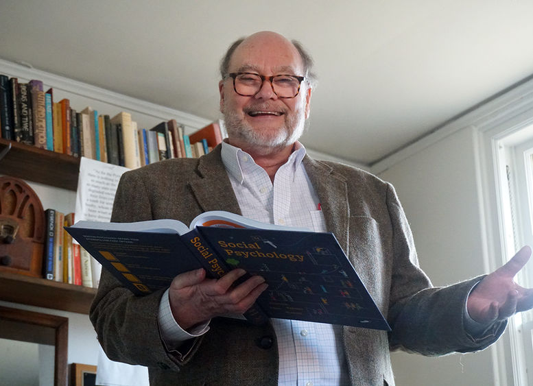 Man holding open text book standing in front of book shelf