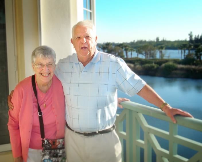 Man and woman standing on a sunny balcony overlooking a river.