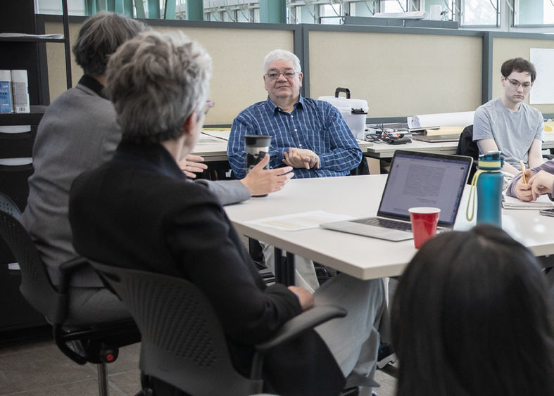A man sitting at a table listening to someone on his right speak as others at the table look on.