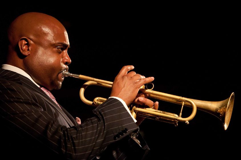 Side profile view of a man in a suit playing a gold trumpet.